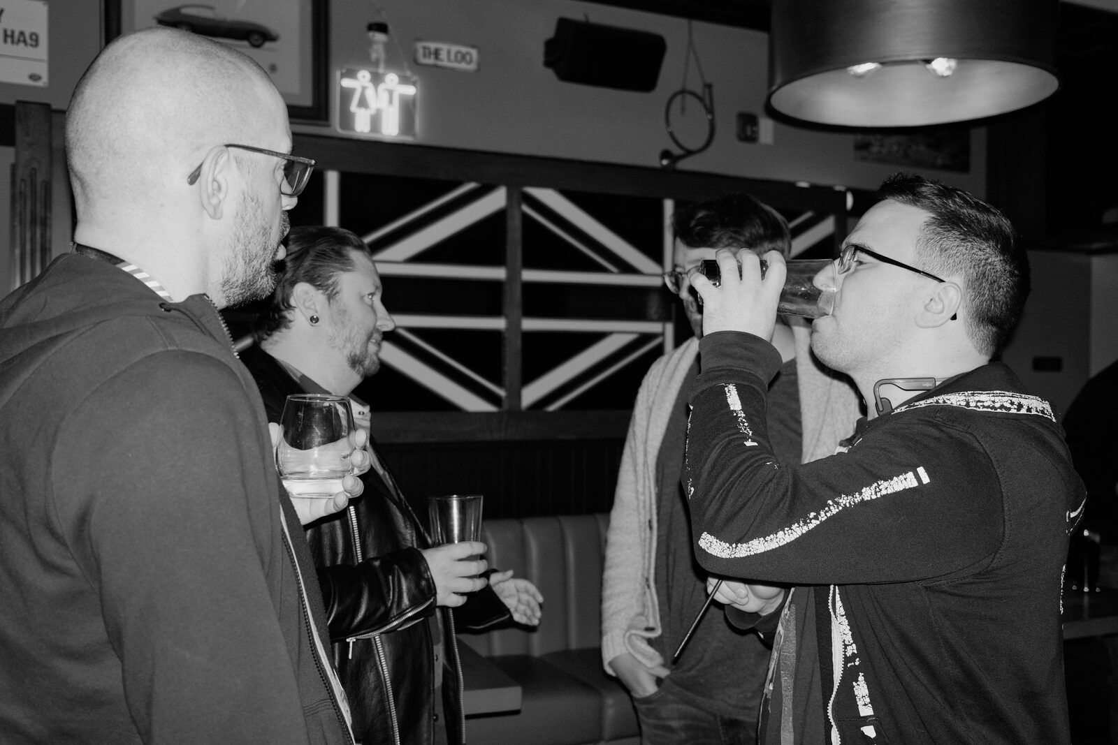 Under a Union Jack panel, an attendee knocks back a drink while three others stand close with pints.
