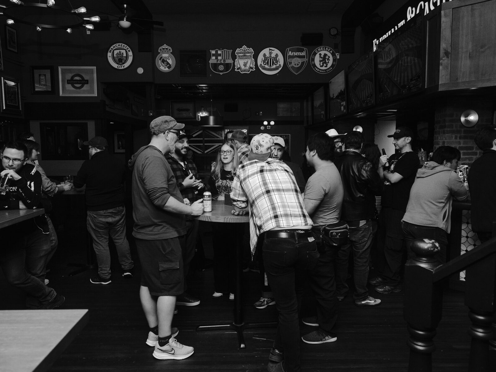 Attendees crowd around high-top tables at the Elephant & Castle, a row of football club crests including Manchester City, Liverpool, Arsenal, and Chelsea along the wall above.