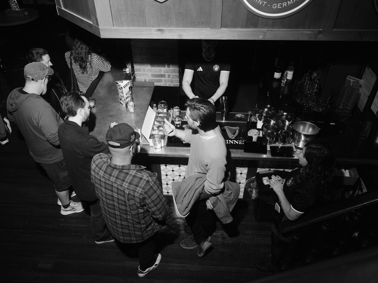 Looking down on attendees lined up at the bar, one leaning in to order from a bartender in front of the Guinness tap mat.