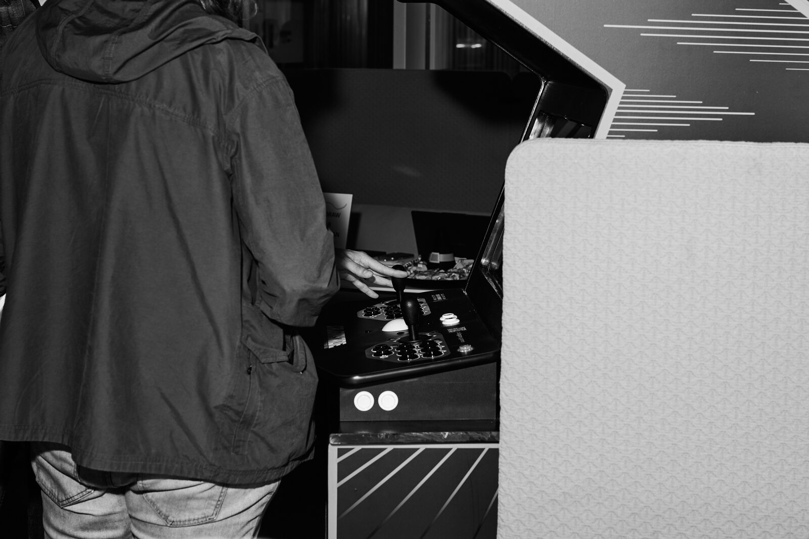 An attendee seen from behind, playing at an arcade cabinet on the showcase floor.