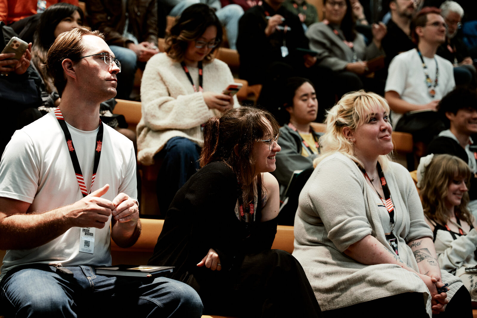Attendees on the wooden bleachers between sessions, lanyards on, a few of them talking and laughing.