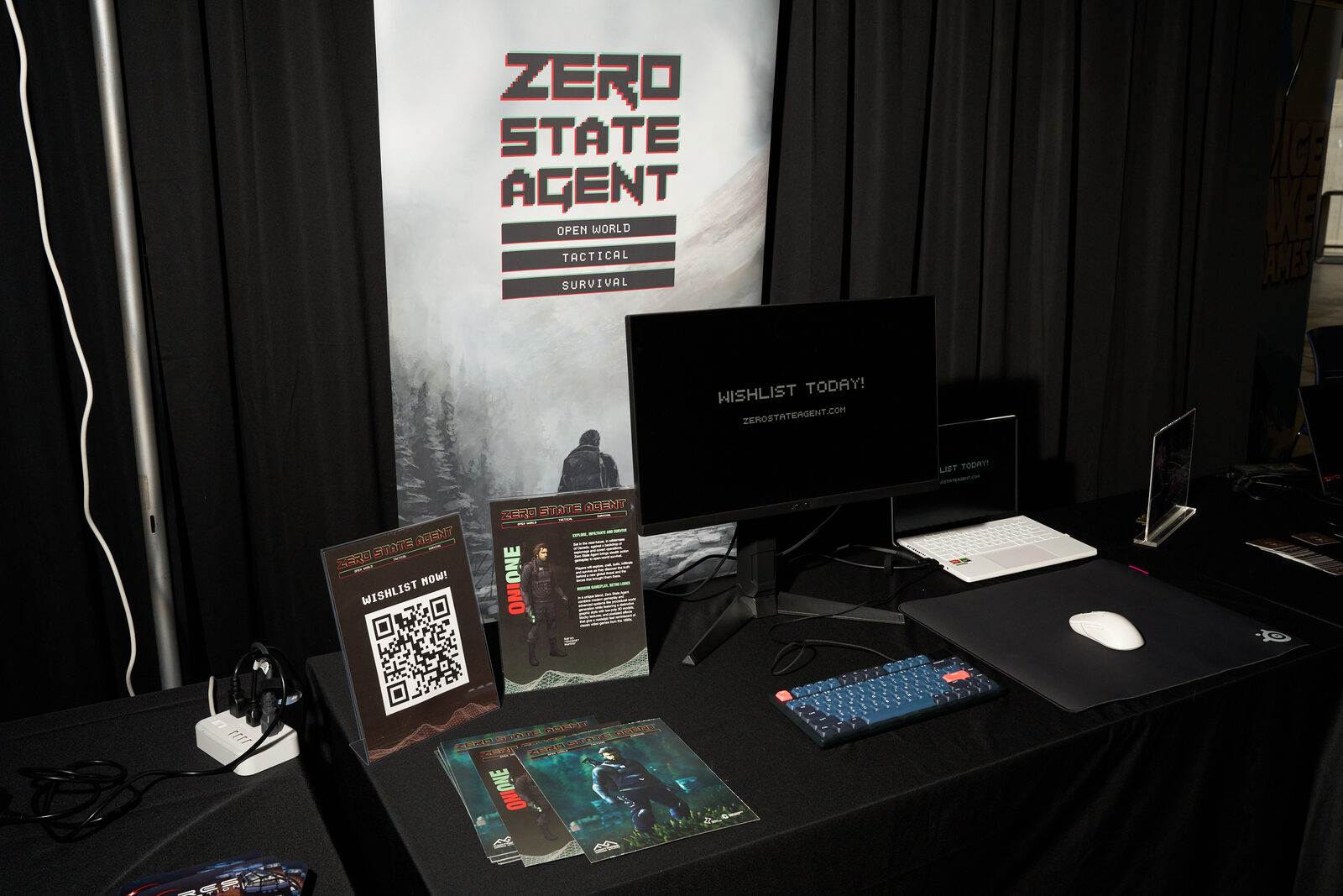 The Zero State Agent booth: banner, a monitor reading "Wishlist today!", QR cards, keyboard and mouse on black cloth.