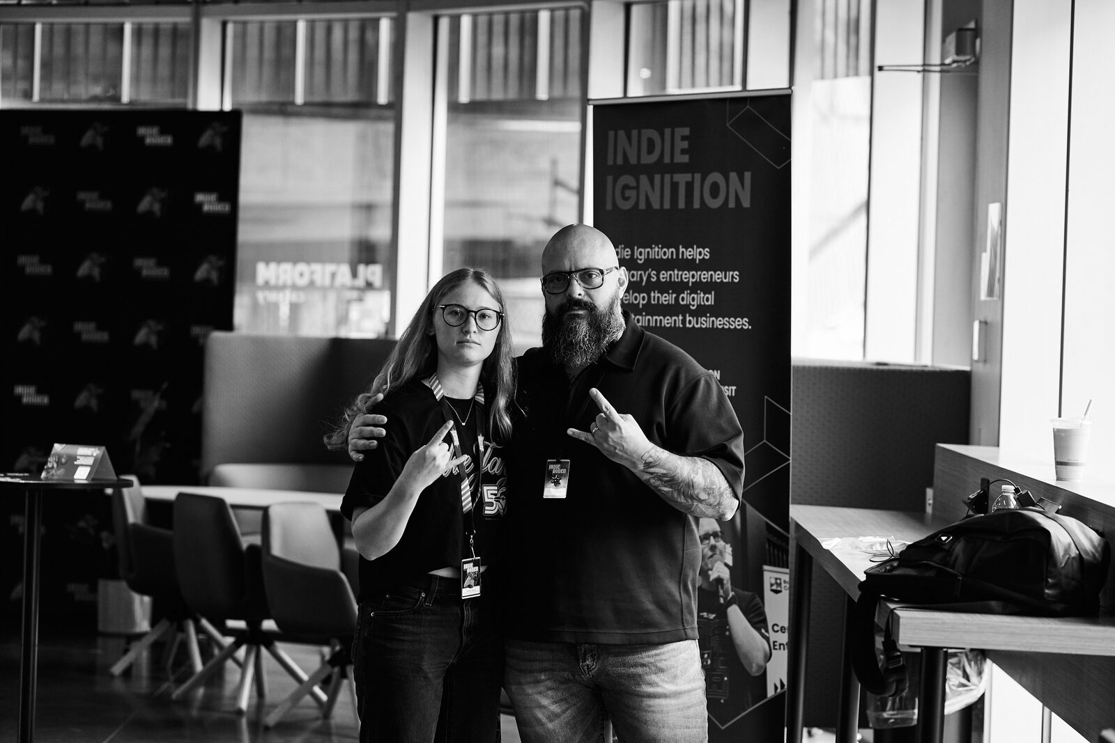 Two attendees throwing metal horns for the camera in front of the Indie Ignition banner.