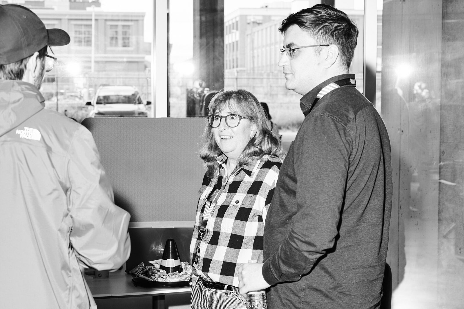 Three attendees talking by the windows, downtown Calgary out on the street behind them.
