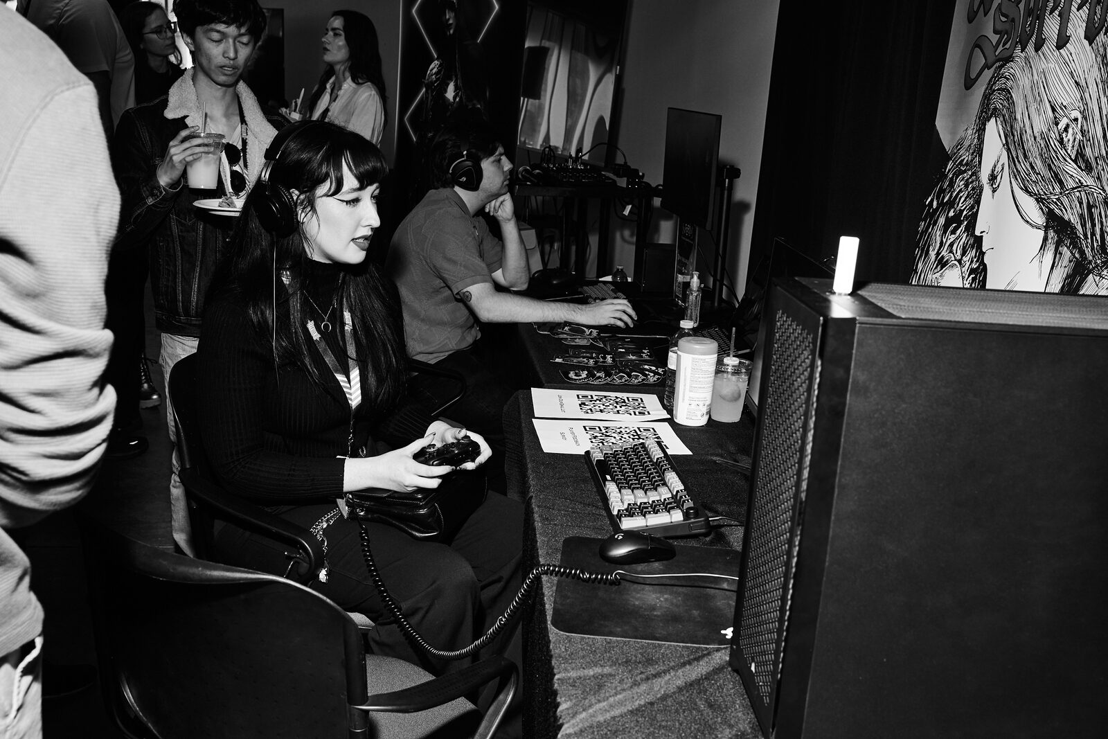 An attendee plays with a controller at a showcase station, headphones on, illustrated key art on the wall behind.