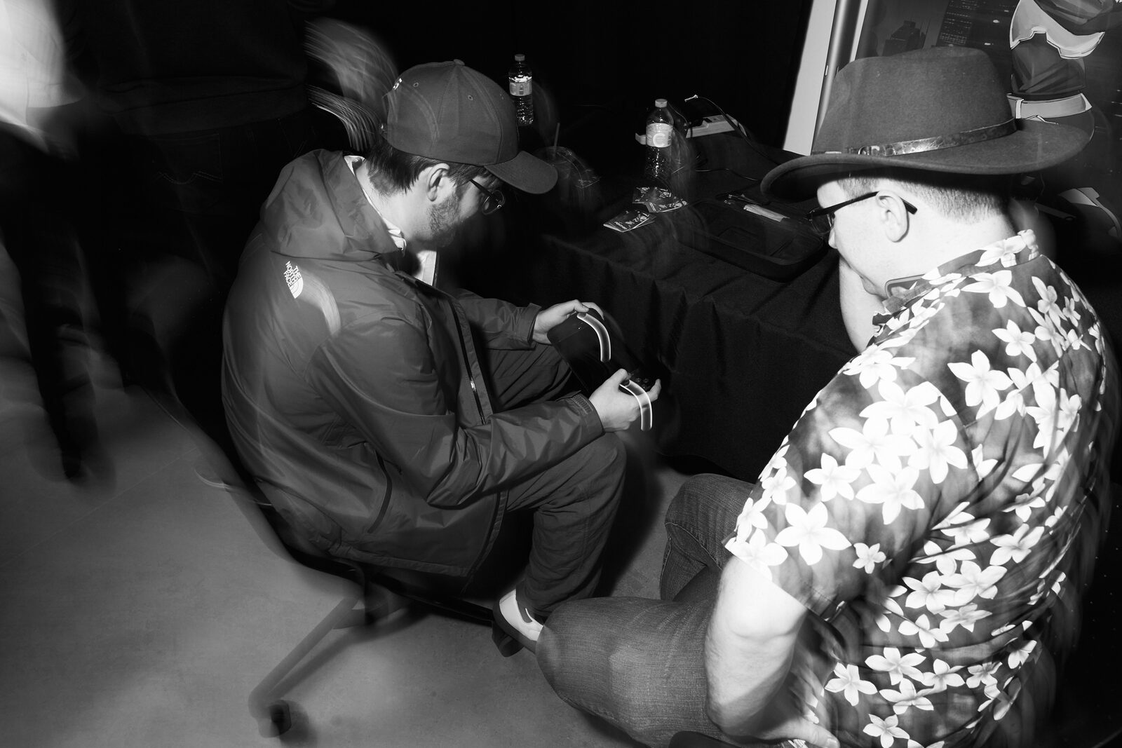 Two attendees seated deep in conversation between stations, one in a cowboy hat and floral shirt.