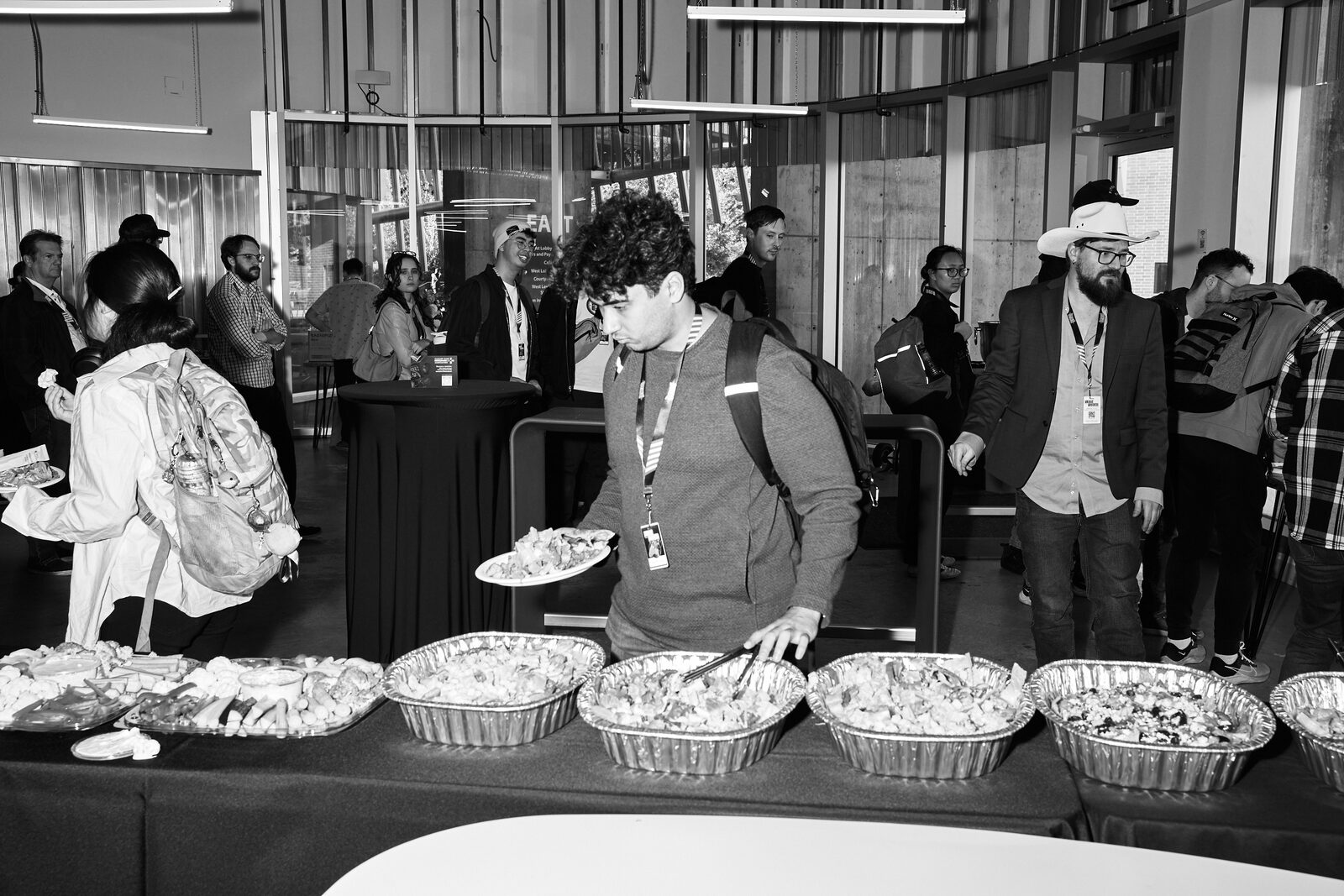 The lunch line in the lobby — attendees serving themselves from foil trays, glass doors and daylight behind.