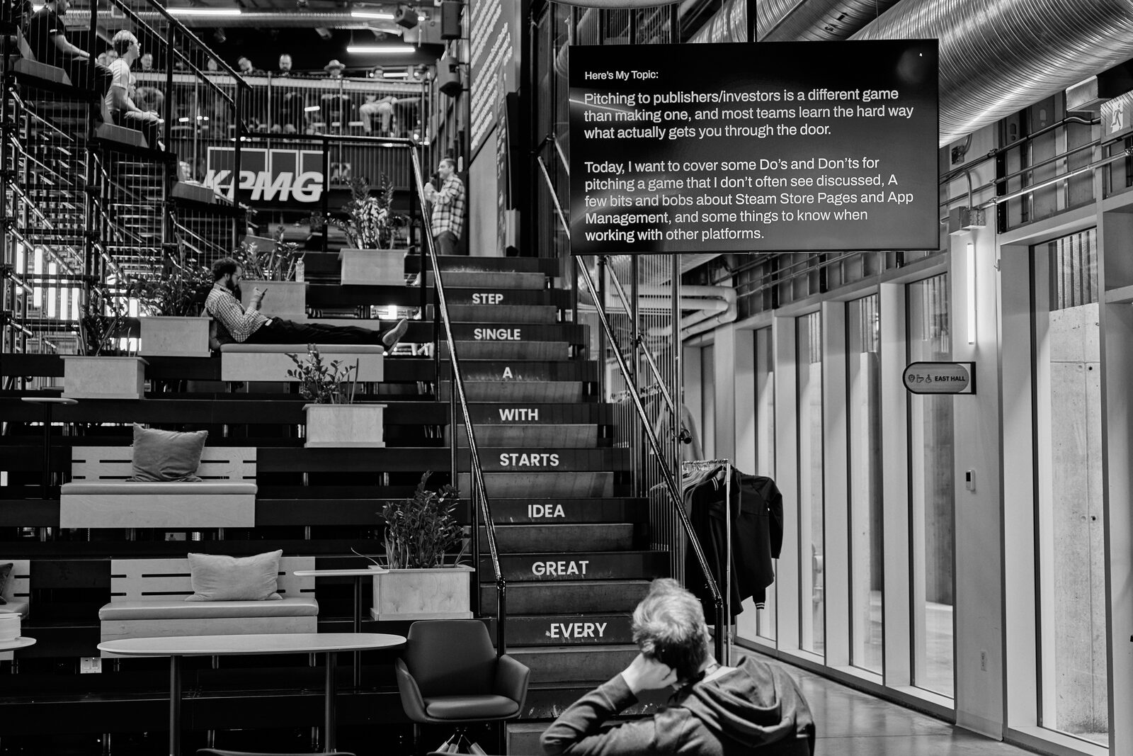 The Platform Calgary stairwell, single words stencilled down the stringer beside the KPMG wall, an attendee reading alone at the bottom.