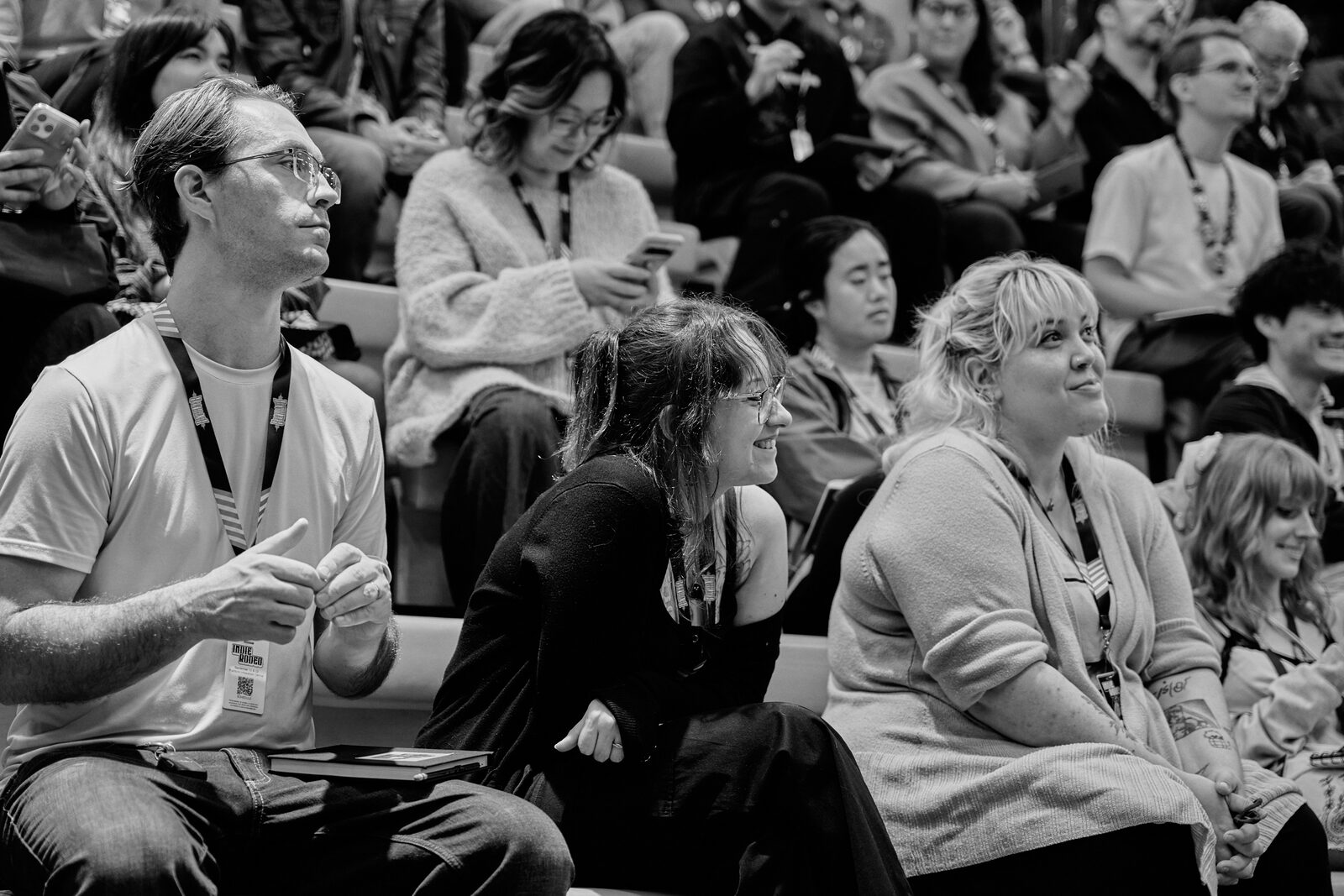 Attendees on the wooden bleachers between sessions, lanyards on, a few of them talking and laughing.