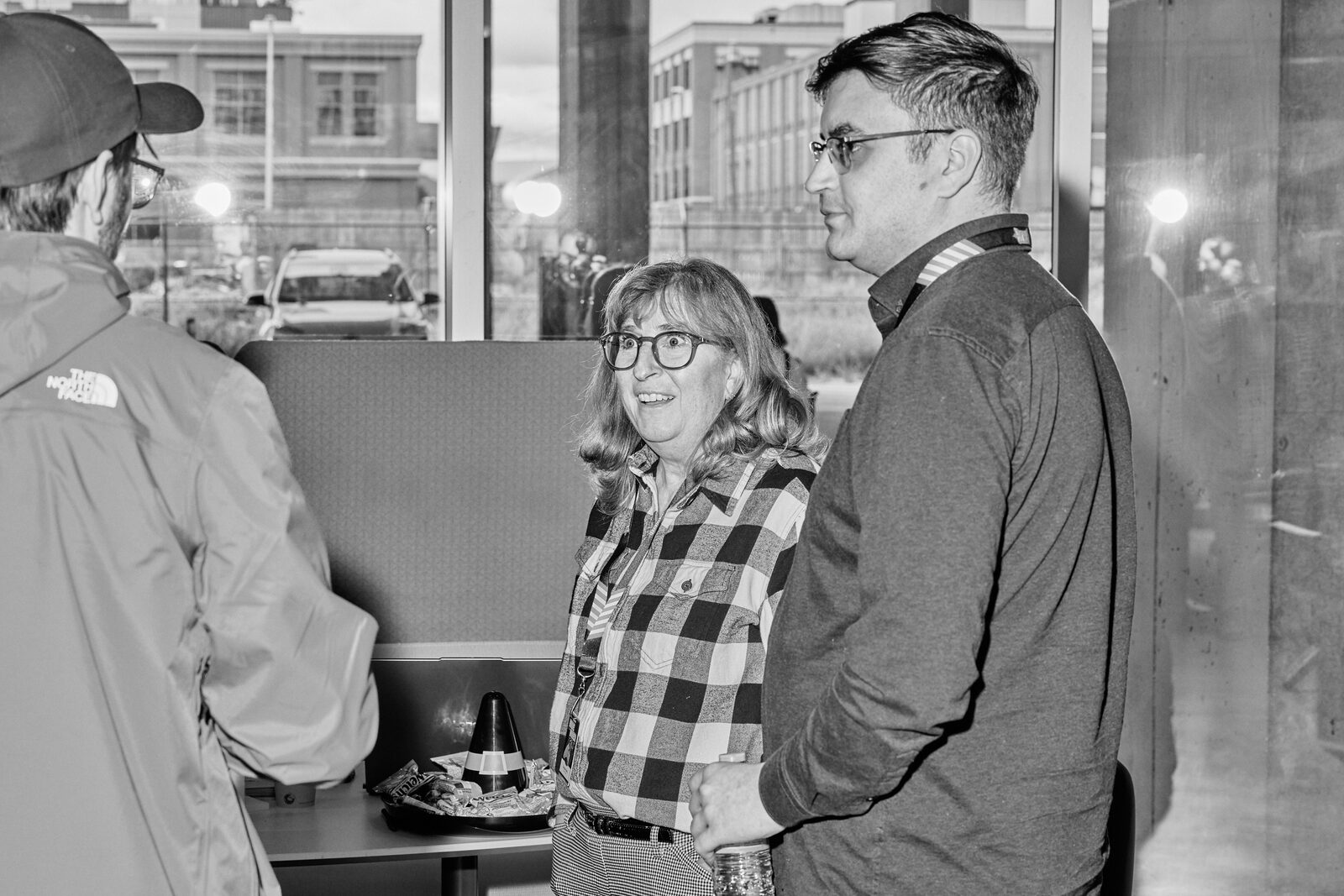 Three attendees talking by the windows, downtown Calgary out on the street behind them.
