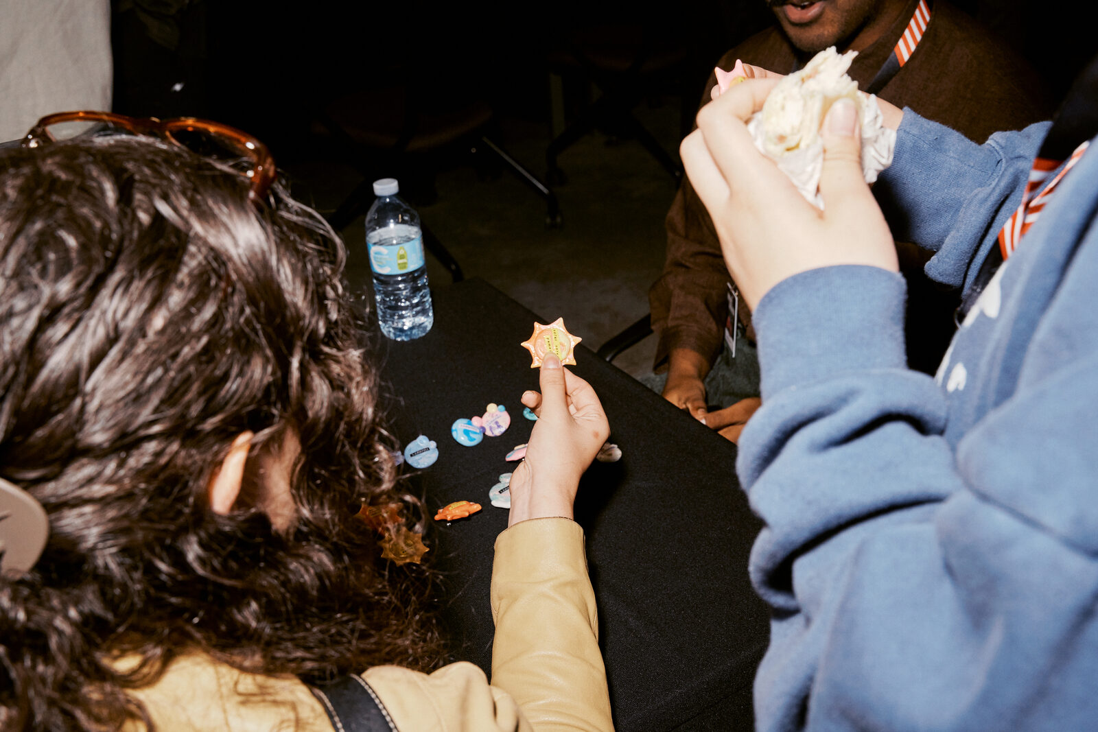Hands over a black cloth trading enamel pins, one holding a yellow star pin up to the light.