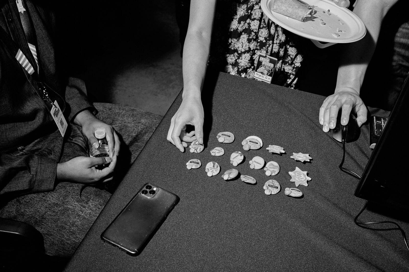 Enamel pins and stickers laid out in rows on a black cloth, two sets of hands sorting through them from opposite sides.