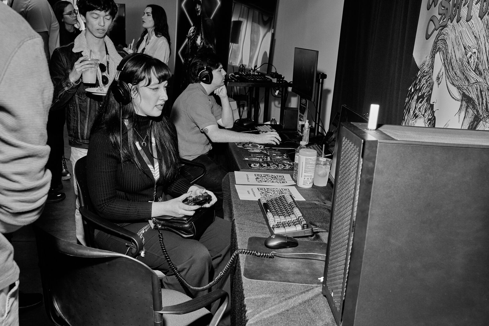 An attendee plays with a controller at a showcase station, headphones on, illustrated key art on the wall behind.