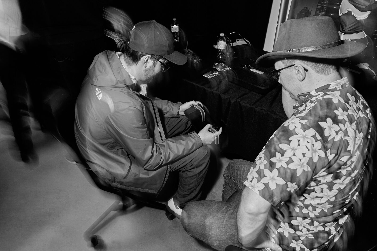 Two attendees seated deep in conversation between stations, one in a cowboy hat and floral shirt.