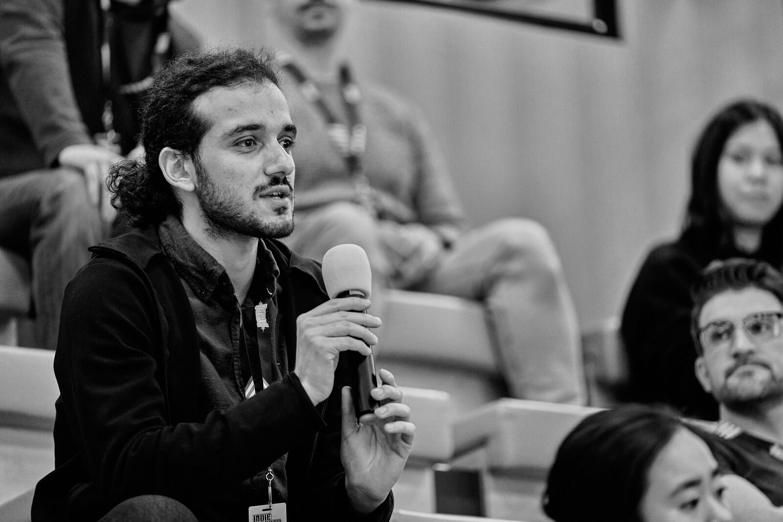 An attendee holds the roving mic to ask a question from the floor, other attendees turned toward him.