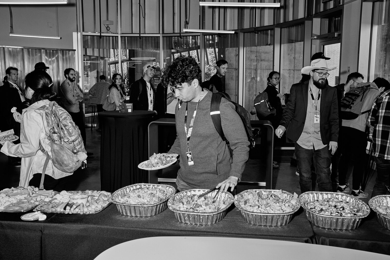 The lunch line in the lobby — attendees serving themselves from foil trays, glass doors and daylight behind.