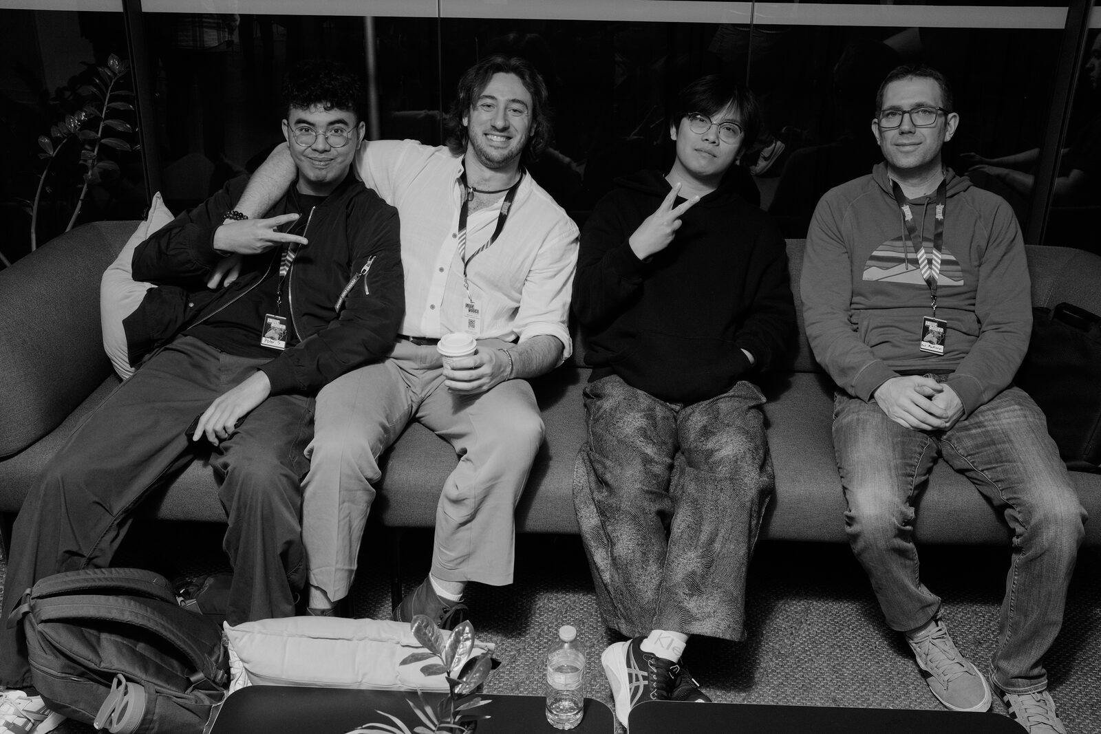 Four attendees with lanyards pose shoulder to shoulder on a grey couch, two throwing peace signs.