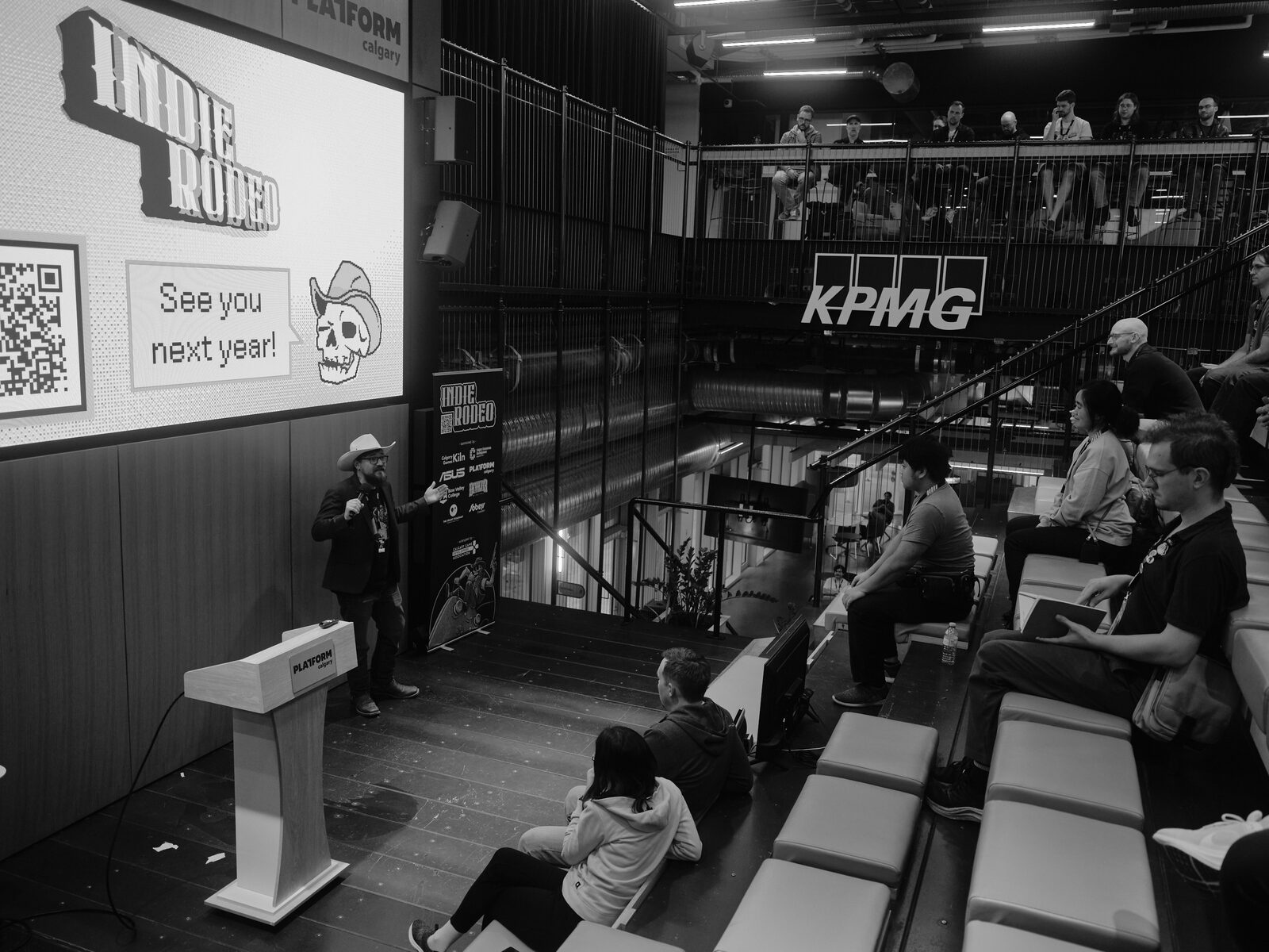 From the balcony, a host in a cowboy hat closes out the day beside a screen showing the Indie Rodeo mascot and "See you next year!", a few attendees still on the bleachers.